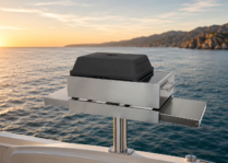 Stainless steel electric grill mounted on a yacht with ocean water, sunrise sky, and distant coastline in the background.