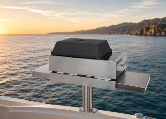Stainless steel electric grill mounted on a yacht with ocean water, sunrise sky, and distant coastline in the background.