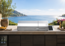 Kenyon Big American Grill built into a luxury outdoor kitchen overlooking the ocean, with stainless steel lid, stone countertop, and coastal entertaining accents.