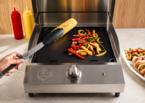 corn and peppers on a black griddle on a portable stainless steel grill