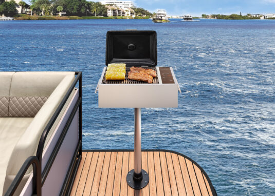 Kenyon stainless steel electric grill with closed black lid, IntelliKEN touch controls, side handles, and pedestal mount on a boat