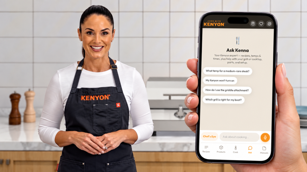 Woman wearing a Kenyon apron in a kitchen beside a hand holding a phone displaying the app’s Ask Kenna assistant for cooking tips and grill support.